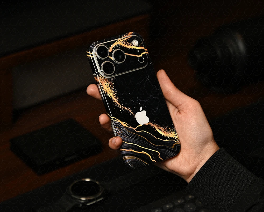 Hand holding a smartphone with a black and gold case, blurred background